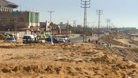 Far-away-shot-of-street-vendor-and-people-on-the-side-of-a-busy-main-road-in-a-city-of-Gaza,-Palestine