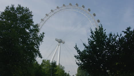 El-Mundialmente-Famoso-London-Eye-Noria,-Punto-De-Referencia-Visto-Desde-Una-Perspectiva-Peatonal-Baja-Detrás-De-Los-árboles-Con-Un-Autobús-Rojo-De-Dos-Pisos-Conduciendo-A-Través