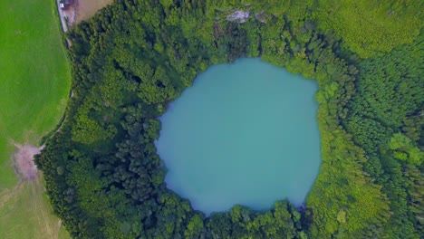 Aerial-drone-view-of-lagoa-do-Congro-blue-turquoise-round-lake-in-middle-of-green-countryside
