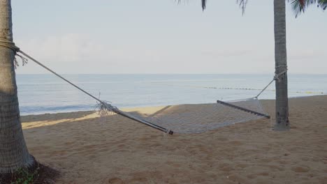 A-swaying-hammock-suspended-between-two-coconut-trees-overlooking-the-beautiful-beach-in-Pattaya,-Chon-Buri,-Thailand