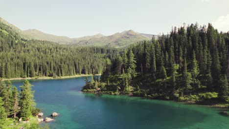 Cinematic-drone-aerial-over-a-beautiful-alpine-mountain-lake-surrounded-by-woods-and-mountain-peaks