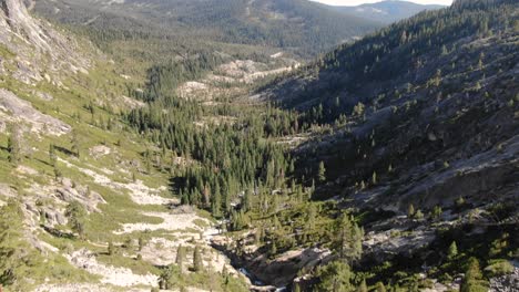 4K-ariel-drone-footage-flying-over-a-mountain-waterfall-in-the-Sierra-Nevada-peaks-and-trees,-rushing-water-from-snow-melt-flows-into-the-American-River-in-Desolation-Wilderness