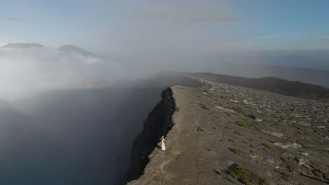 Blond-angelic-woman-in-white-dress-walks-along-Ijen-volcano-crater-edge