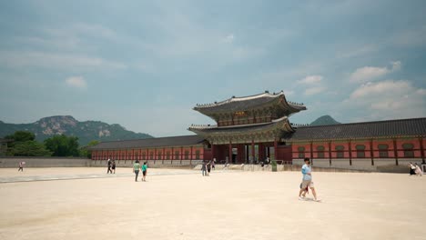 Heungnyemun-Gate-with-Bukhansan-mountain-in-background-against-blue-sky-in-Gyeongbokgung-Palace,-people-torists-walking-,-Seoul,-South-Korea