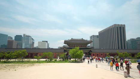 Recorrido-De-Viaje-Grupo-De-Personas-Mayores-Pasó-La-Puerta-Heungnyemun-Y-Cruzó-El-Puente-Yeongjegyo-En-El-Palacio-Gyeongbokgung-Con-Vistas-Al-Edificio-Del-Gobierno-De-Seúl-Y-Rascacielos-Contra-El-Cielo-Azul