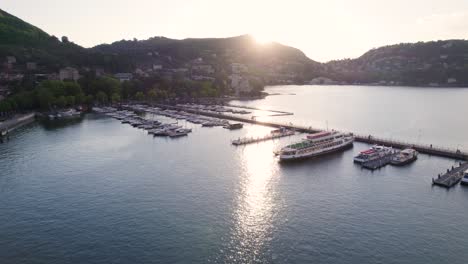 Barcos-Atracados-En-El-Muelle-Del-Lago-De-Como-Con-Destellos-De-Sol-Al-Atardecer---Antena