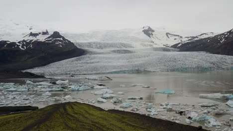 Islandgletscher-Mit-Grünen-Hügeln-Und-Blauem-Eis-Mit-Heranziehendem-Drohnenvideo