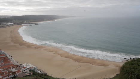 Panning-shot-panoramic-view-of-horizon-at-Nazare-beach-coastline-and-town-from-viewpoint-at-cliff
