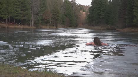 Extremes-Abenteuer,-Während-Eine-Frau-In-Einem-Loch-Schwimmt,-Das-In-Die-Gefrorene-Oberfläche-Des-Sees-Geschnitten-Wurde,-Dann-Auf-Einem-Eisvorsprung-Ruht-Und-Lächelt