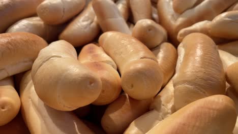 Many-European-buns-bread-sticks-on-top-of-each-other-in-store,-close-up-pan