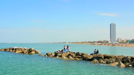 Turistas-Disfrutando-De-Un-Recorrido-Diurno-En-Un-Camino-Rocoso-Junto-Al-Mar-En-Cesenatico,-Italia---Plano-Amplio