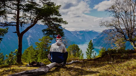 Aufnahme-Eines-Jungen-Mannes,-Der-Auf-Einem-Toten-Baum-Sitzt-Und-An-Einem-Bewölkten-Tag-Die-Malerische-Aussicht-Auf-Den-Fjord-Entlang-Der-Wunderschönen-Bergkette-In-Norwegen-Genießt