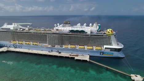 órbita-Aérea-Sobre-El-Crucero-Odyssey-Of-The-Seas-Parado-En-El-Muelle-Con-Un-Océano-Abierto-Detrás