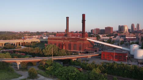 Amplia-Toma-Aérea-De-Empuje-De-Una-Fábrica-De-Ladrillos-En-La-Ciudad-De-Kansas,-Missouri,-Mientras-Pasa-Un-Tren-De-Carga-Al-Atardecer