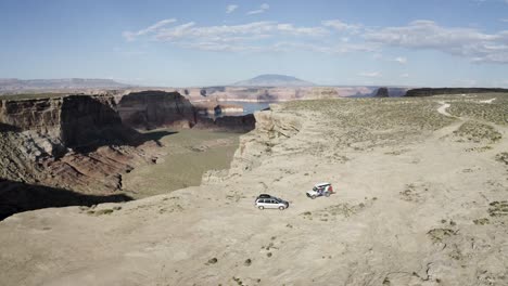 Green-River-overlook-with-two-exploration-vehicles-meeting-near-the-ledge-of-the-canyon,-Aerial-tilt-down-approach-shot