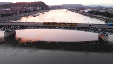 Following-Yellow-Tram-in-Budapest,-Petőfi-Bridge-In-Beutiful-Sunset-Overt-the-Danube-River