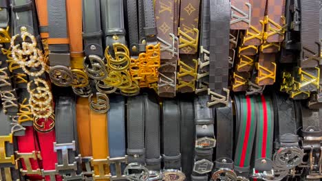 High-quality-fake-designer-belts-hanging-in-Turkey-store,-fake-luxury-brand-belts,-knock-off-superfakes-of-gucci,-hermes,-dior-and-louis-vuitton,-4K-shot