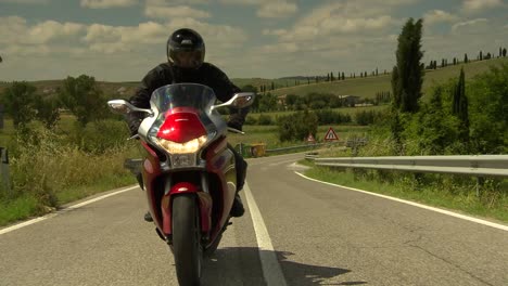 Man-riding-a-motorbike-to-a-beautiful-country-estate-in-Tuscany-in-bright-sunshine-on-a-long-road