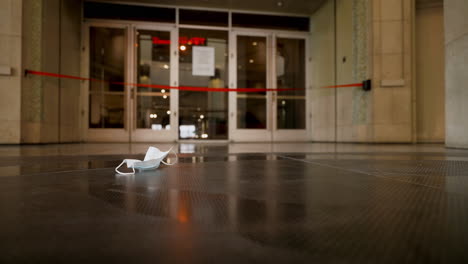 A-Lone-Paper-Face-Mask-Lays-on-the-Floor-of-a-Mall-During-the-Covid-19-Pandemic