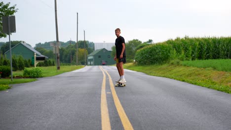 Plano-Bajo-De-Un-Adolescente-Montando-Patineta-En-Medio-De-Una-Carretera