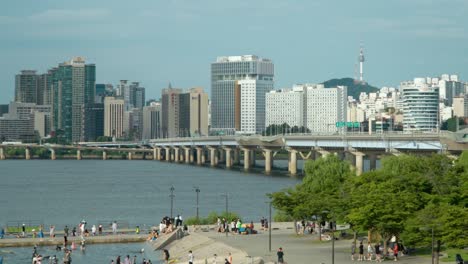Zoom-in-from-Yeouido-Hangang-Park-Kids-Water-Playground-to-Mapo-Bridge-over-Han-river-and-Seoul-cityscape---Aerial-view