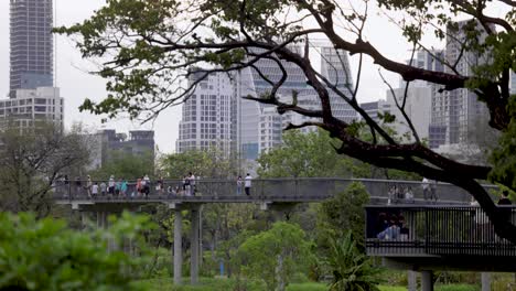 Closeup-of-Tourists-walking-on-the-elevated-footbridge-in-the-urban-Benjakitti-Park-or-Benchakitti-Forest-Park-enjoying-the-view-of-the-green-lung-of-Bangkok,-Thailand,-50fps