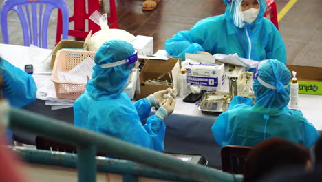Eine-Gruppe-Medizinischer-Mitarbeiter-In-Blauem-Psa-anzug,-Die-Covid-19-impfstofffläschchen-Und-Spritzen-In-Der-Gebäudehalle-In-Vietnam-Halten