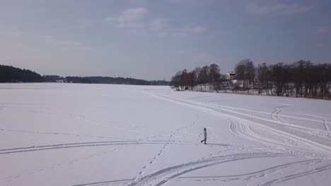 Smooth-panning-wide-aerial-shot-of-blonde-female-walking-on-massive-frozen-lake