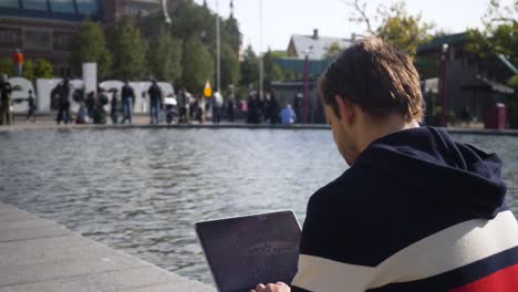 Nett-Aussehender-Junger-Mann,-Der-Am-Museumplein-In-Amsterdam-Sitzt-Und-An-Einem-Sonnigen-Tag-Auf-Dem-Laptop-Tippt