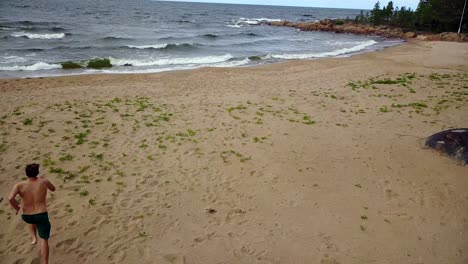 AERIAL,-male-friends-on-beach-running-to-the-water