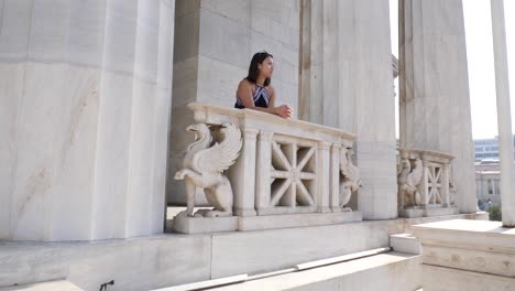 Shot-of-a-young-asian-woman-who-leans-on-a-balcony-of-an-old-marble-building-in-Athen