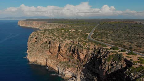 Drone-footage-flying-towards-the-cliffs-and-a-nearby-road-with-cars-driving-on-it-in-the-background