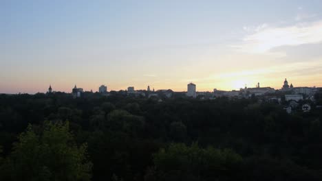 Panning-shot-of-the-skyline-of-a-city-at-sunset,-with-lots-of-trees-in-the-foreground