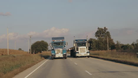 Zwei-Peterbilt-Semi-Achtzehnrad-LKWs-Fahren-In-Zeitlupe-Nebeneinander-In-Der-Abendsonne-Die-Autobahn-Hinunter