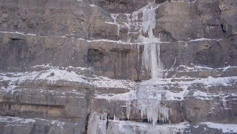 A-frozen-waterfall-along-a-shear-cliff-in-a-winter-scene---panning-up