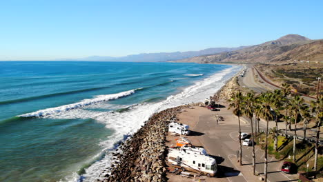 Aerial-drone-shot-of-a-California-beach-paradise-with-blue-ocean-waves-crashing-against-a-palm-tree-lined-beach-in-Ventura