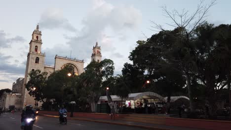 Pushing-in-to-the-Catedral-de-San-Ildefonso,-Merida,-Yacatan,-Mexico-at-dusk-with-vendors-set-up-in-the-grand-plaza