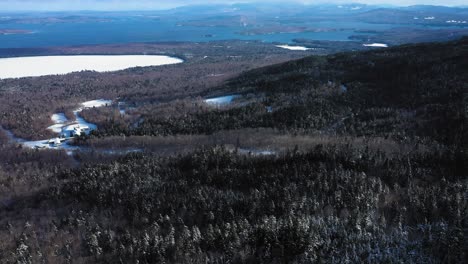 Aerial-footage-flying-down-the-slope-of-a-snowy-mountain-towards-a-small-frozen-lake-and-a-large-lake-with-open-water