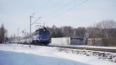 Medium-wide-shot-of-an-electric-passenger-train-passing-through-a-town-covered-with-snow-during-winter-in-daytime
