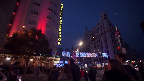 Toma-Panorámica-Desde-Detrás-De-La-Pared-Para-Revelar-El-Letrero-Iluminado-Del-Hotel-Emperador-En-El-Costado-De-La-Propiedad-Mientras-La-Gente-Pasa-Caminando-Por-La-Acera-Debajo-En-La-Noche-Oscura