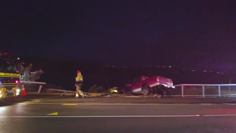 Panorámica-A-Través-De-La-Escena-Del-Accidente-En-La-Carretera,-Los-Bomberos-Caminan-Alrededor-Del-Automóvil-Que-Se-Estrelló-Contra-La-Cerca