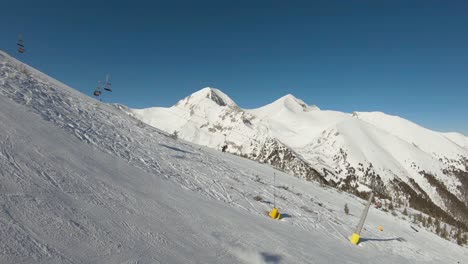 Skier-skiing-on-a-slope-with-ski-lift-and-top-of-a-mountain-in-the-background-on-a-sunny-day