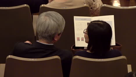 Spectators-sitting-at-a-concert-hall-with-a-program-in-their-hands