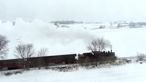 Aerial-long-shot-of-restored-steam-engine-pulling-passenger-cars-through-the-snow-covered-landscape