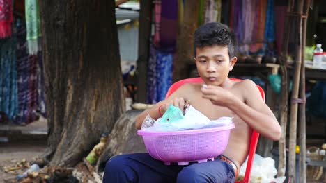 Vendedor-Infantil-Comiendo-Fruta-En-El-Mercado-Local-Durante-El-Descanso-En-Siem-Reap,-Camboya
