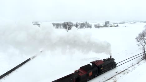 Aerial-pass-over-a-restored-steam-engine-pulls-passenger-cars-through-snowy-Amish-country-Strasburg-Railroad-Ronks,-Lancaster-County-Pennsylvania-Concept:-railroads,-traditional,-winter,-Polar-Express