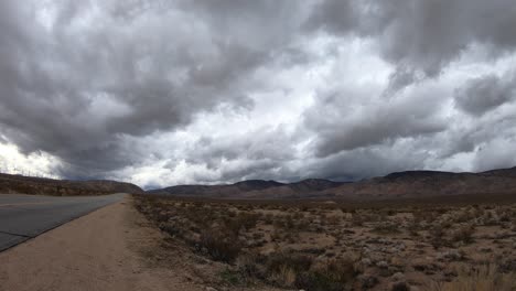 TIME-LAPSE,-Dark-storm-clouds-rolling-over-Mojave-Desert-mountains-by-road