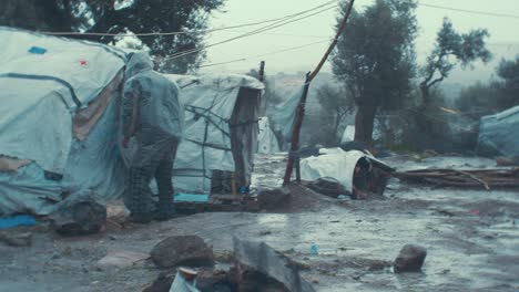 Old-man-refugee-fixing-his-shelter-tent-in-the-'Jungle'-Olive-Grove-of-Moria-Refugee-Camp-during-bleak-weather-dire-conditions-WIDE-PAN-SHOT
