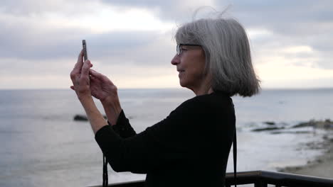 An-old-lady-on-vacation-happy-and-smiling-while-taking-a-picture-of-the-city-and-ocean-in-Laguna-Beach,-California-SLOW-MOTION