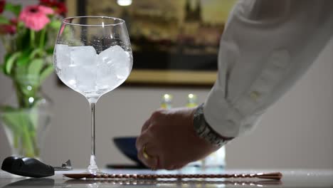 Pouring-two-shots-of-dark-blue-gin-into-a-large,-stemmed-balloon-glass-full-of-ice